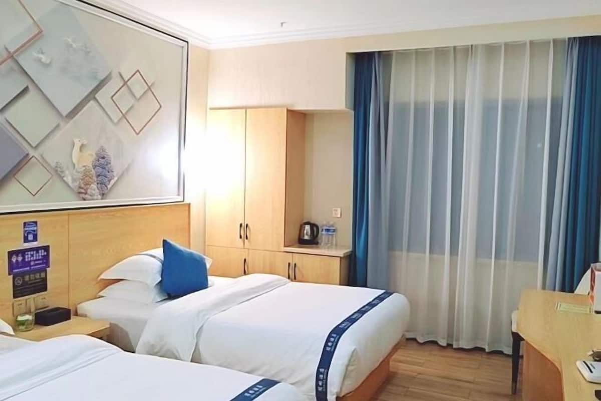 Habitación de hotel con dos camas, un escritorio, un espejo, un armario y un ventanal con cortinas.
