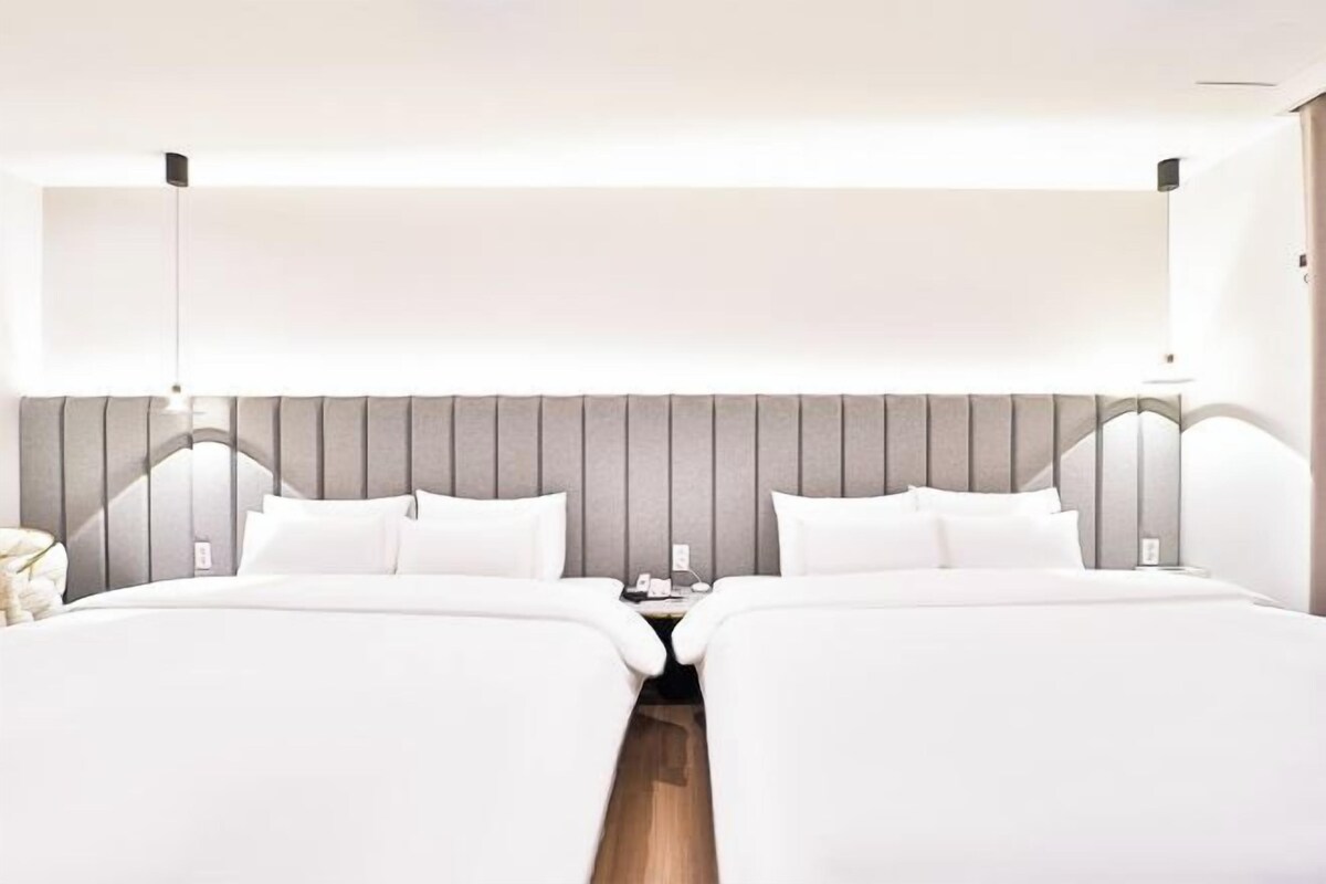Una habitación de hotel moderna con una cama grande, dos mesitas de noche y una paleta de colores neutros.