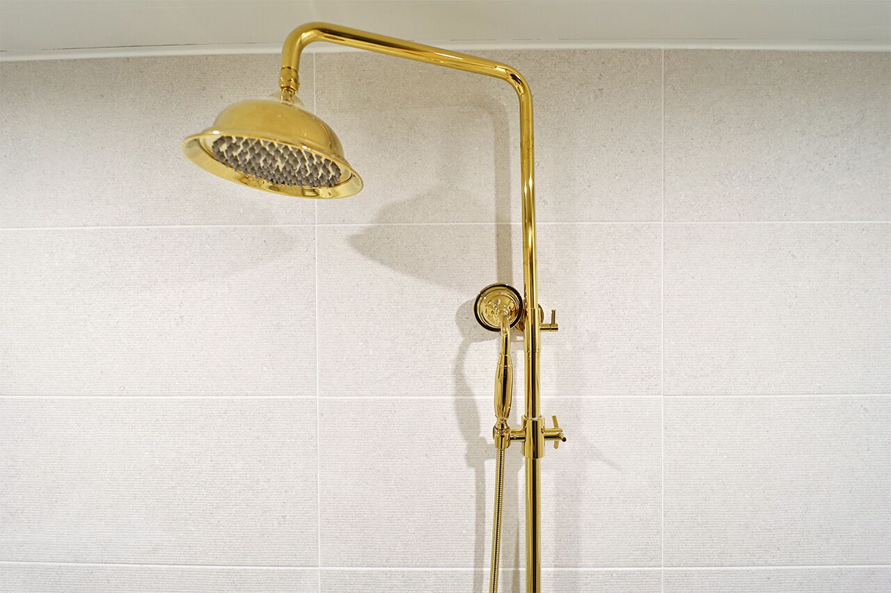 A gold showerhead with a curved handle and a separate handheld shower attachment.