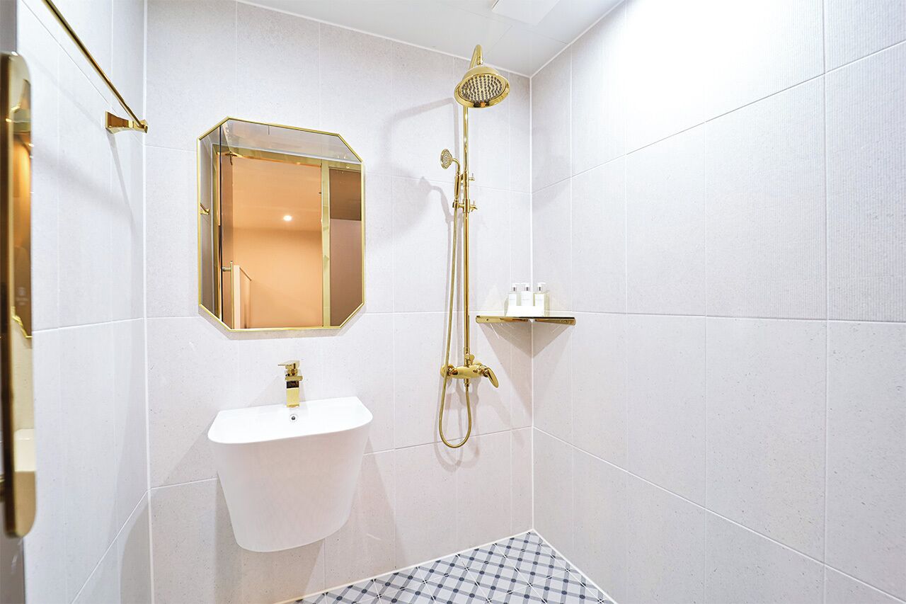 Casa de banho com lavatório branco, chuveiro dourado e espelho com moldura dourada.