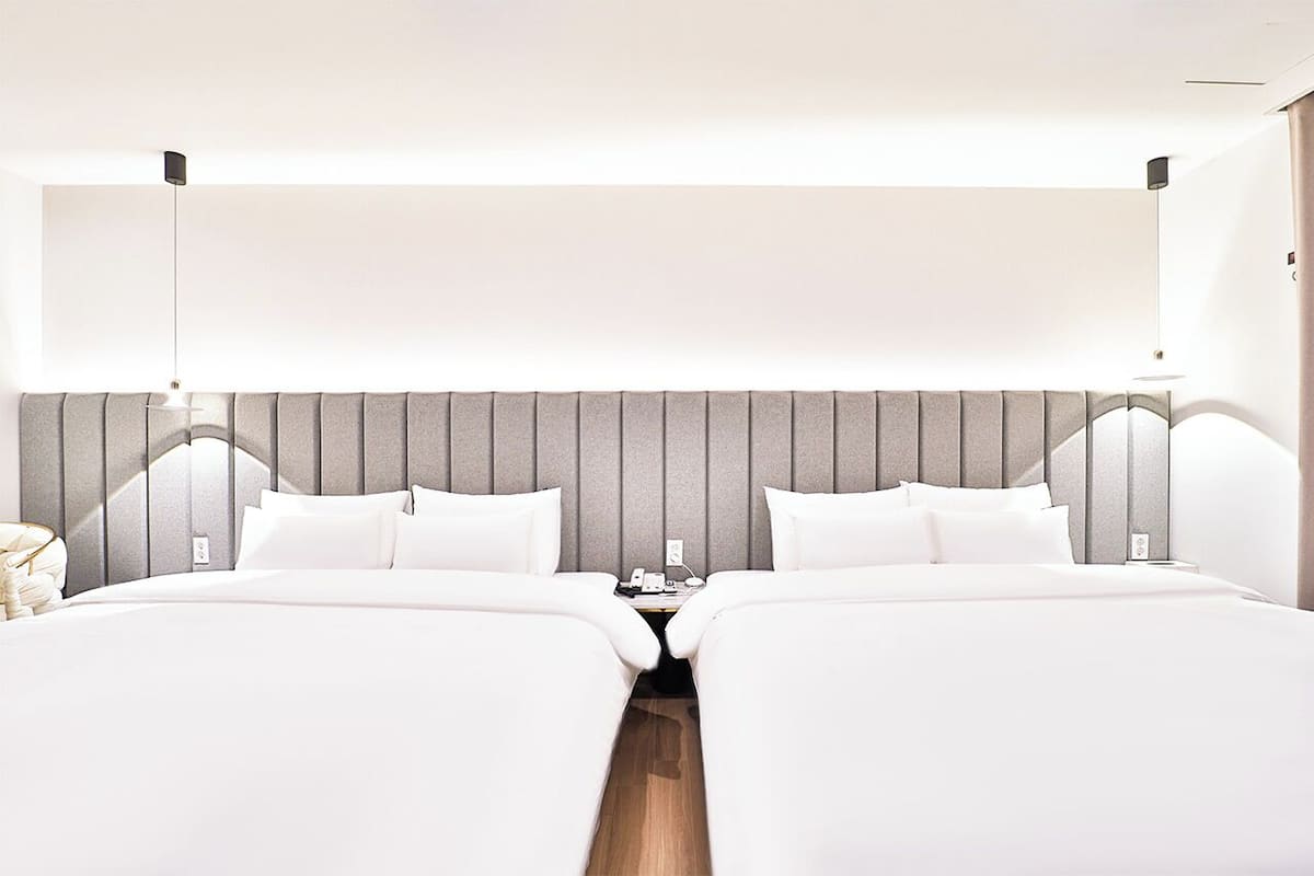 Una habitación de hotel moderna con una cama grande, dos mesitas de noche y un cabecero de tonos neutros.