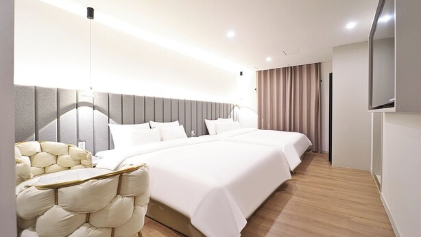 A modern hotel room with a large bed, a seating area with a cushioned chair, and a flat-screen TV mounted on the wall. - HADAN DENBASTA HOTEL (Busan)
