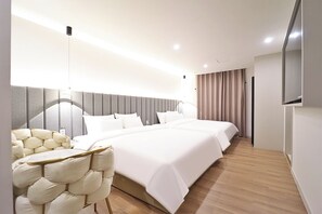 Une chambre d’hôtel moderne dotée d’un grand lit, d’un coin salon avec un fauteuil confortable et d’un téléviseur à écran plat fixé au mur.