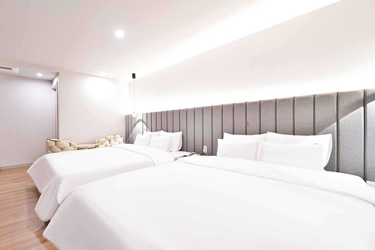 Moderni hotellihuone, jossa on kaksi sänkyä, suuri ikkuna ja yöpöytä, jossa on lamppu.
