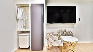 A compact living space with a built-in refrigerator, a flat-screen TV mounted above a dining area, and a small trash bin. - HADAN DENBASTA HOTEL (Busan)