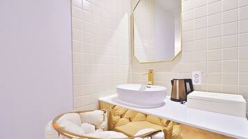 A modern bathroom with white tiles, a gold-framed mirror, a white sink, and a gold-framed vanity.