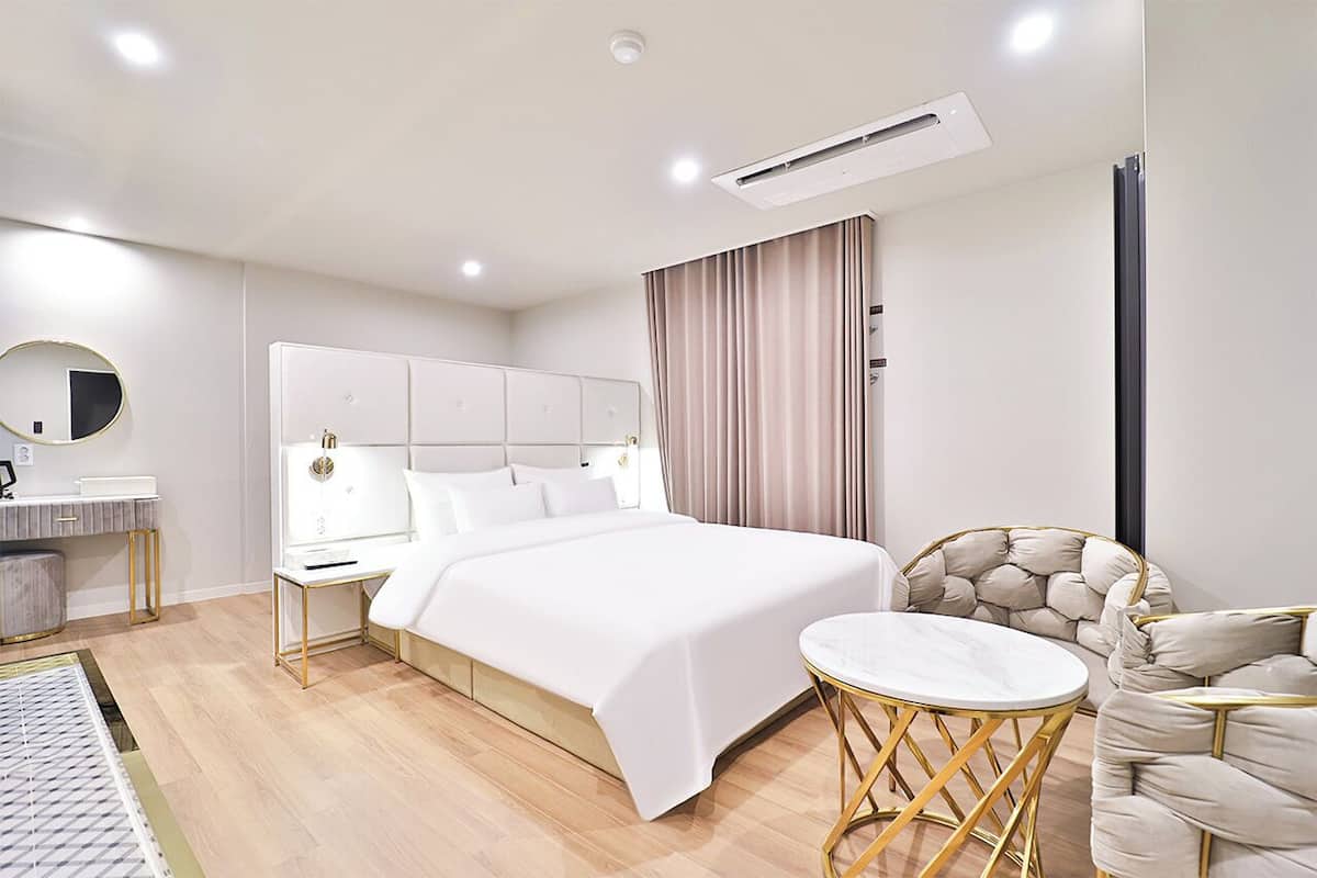 Una habitación de hotel moderna con una cama grande, mesitas de noche, una mesa redonda y un sillón cómodo.