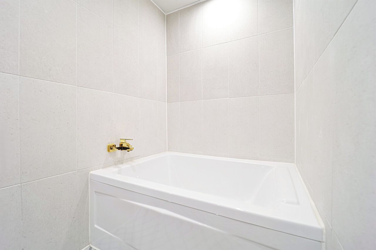 A white bathtub in a corner with white tiled walls and a gold faucet.