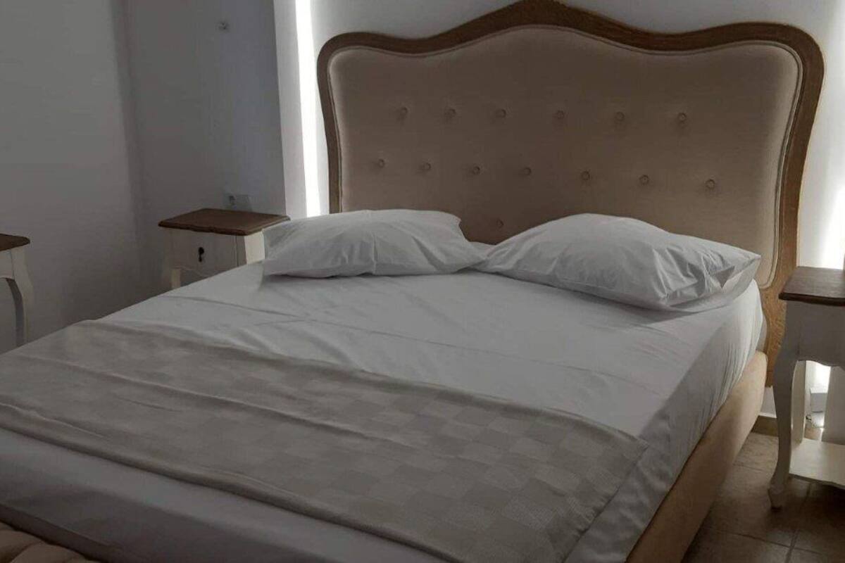 Una cama bien hecha con cabecera de madera, ropa de cama blanca y dos mesitas de noche con cajones.
