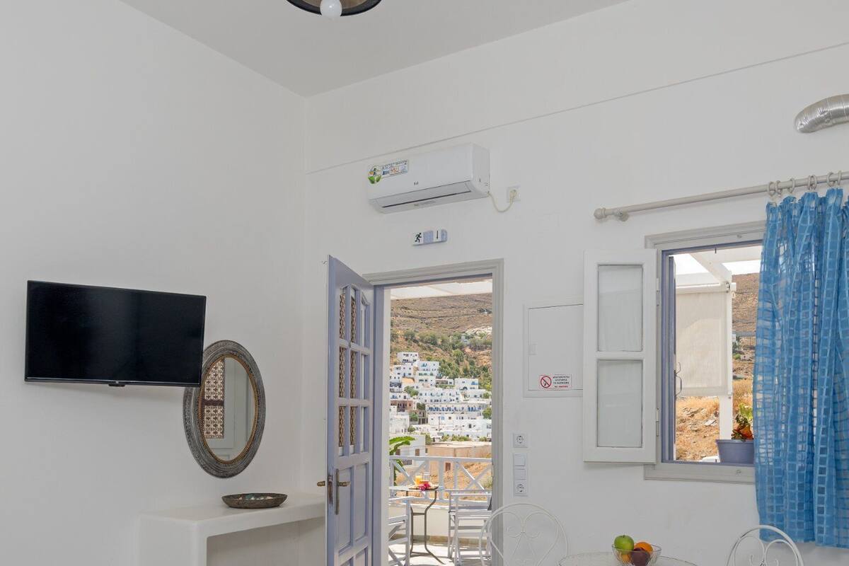 Una habitación con cama, televisión, espejo, ventana con cortinas, mesa y sillas, y aire acondicionado.