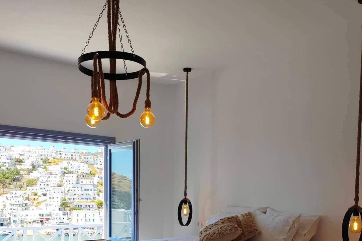 Un dormitorio moderno con cama curva, lámparas colgantes y vistas a un pueblo costero.