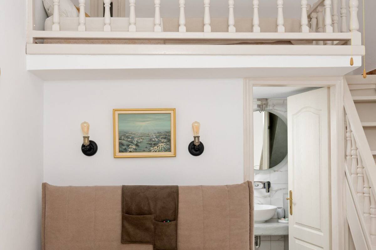 Un dormitorio con una cama litera, un cabecero, un cuadro y un baño visible a través de una puerta abierta.