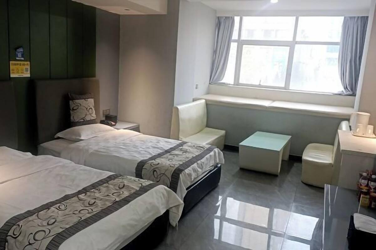 Habitación de hotel con dos camas, una mesita, un banco y una ventana con cortinas.
