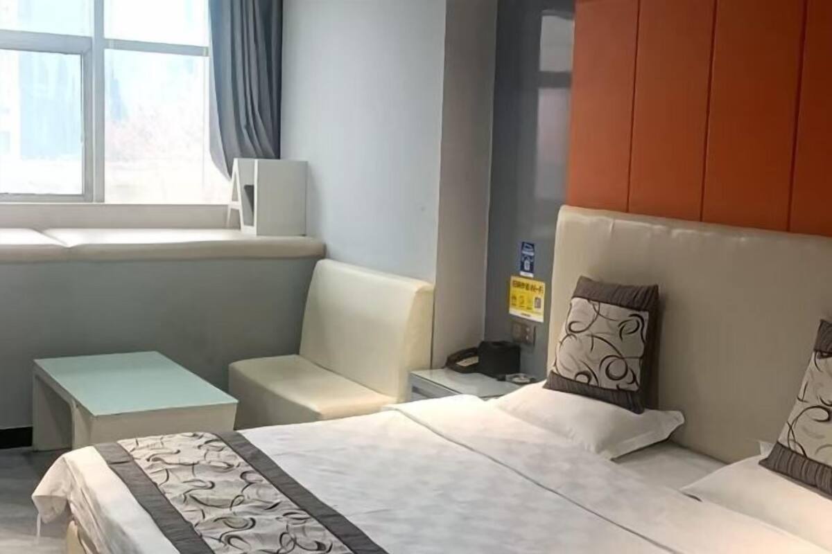 Una habitación de hotel con una cama, una mesita pequeña, un sofá, una ventana con cortinas y un teléfono en la pared.