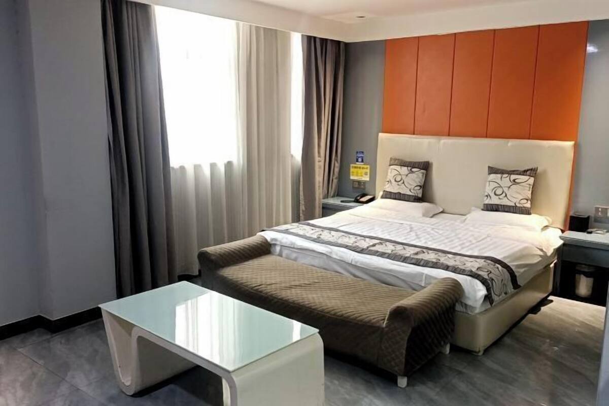 Una habitación de hotel moderna con una cama grande, una mesita de noche, un escritorio pequeño y una ventana con cortinas.