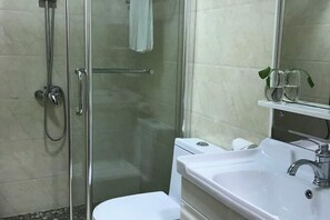 Une salle de bain avec une douche à parois de verre, des toilettes blanches, un lavabo avec un miroir et une petite étagère sur laquelle reposent deux verres.