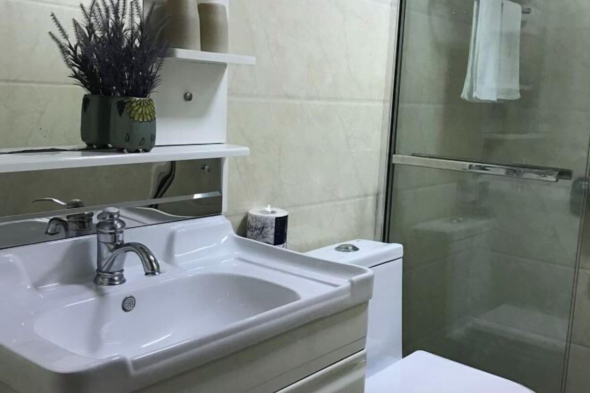 Une salle de bain avec un lavabo blanc, un miroir, des toilettes et une cabine de douche en verre.