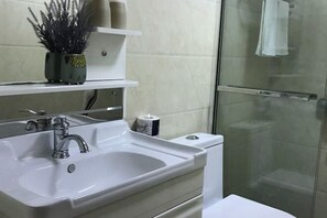 Une salle de bain avec un lavabo blanc, un miroir, des toilettes et une cabine de douche en verre.
