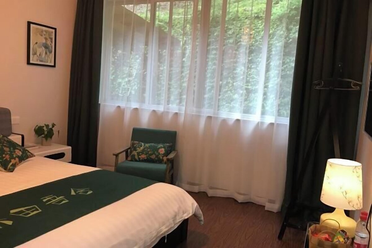 Une chambre d’hôtel avec un lit, une chaise, une lampe et une fenêtre avec des rideaux.