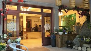 Een hotelingang met een houten deur, kamerplanten en een zithoek met een tafel en stoelen.