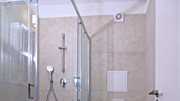 Une salle de bain moderne dotée d’une douche à parois de verre, de toilettes et d’un sèche-mains.