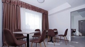Una sala de reuniones moderna con una gran mesa y seis sillas, ventanas amplias con cortinas, y una puerta visible a la derecha.
