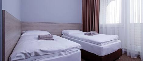 A hotel room with two beds, a wooden headboard, a large window with sheer curtains, and a brown carpet.