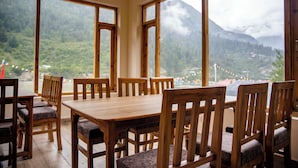 Ein Essbereich mit Holztischen und -stühlen, große Fenster mit Blick auf die Berge.