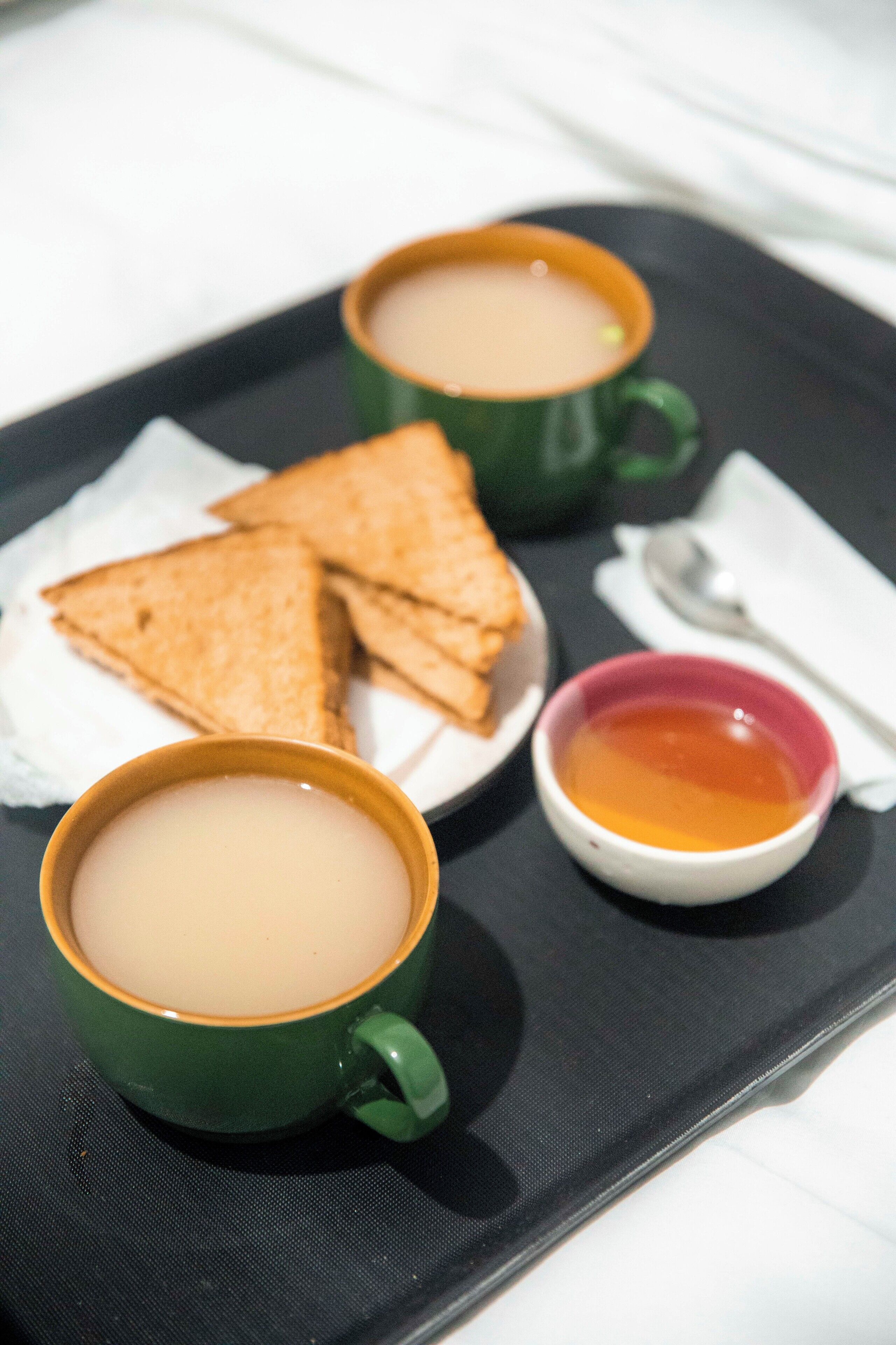 A tray with two green cups of tea, a small bowl of jam, and three triangular sandwiches.