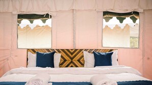 Ein Bett mit einem gemusterten Kopfteil, zwei mit Vorhängen versehene Fenster und zusammengerollte Handtücher auf dem Bett.