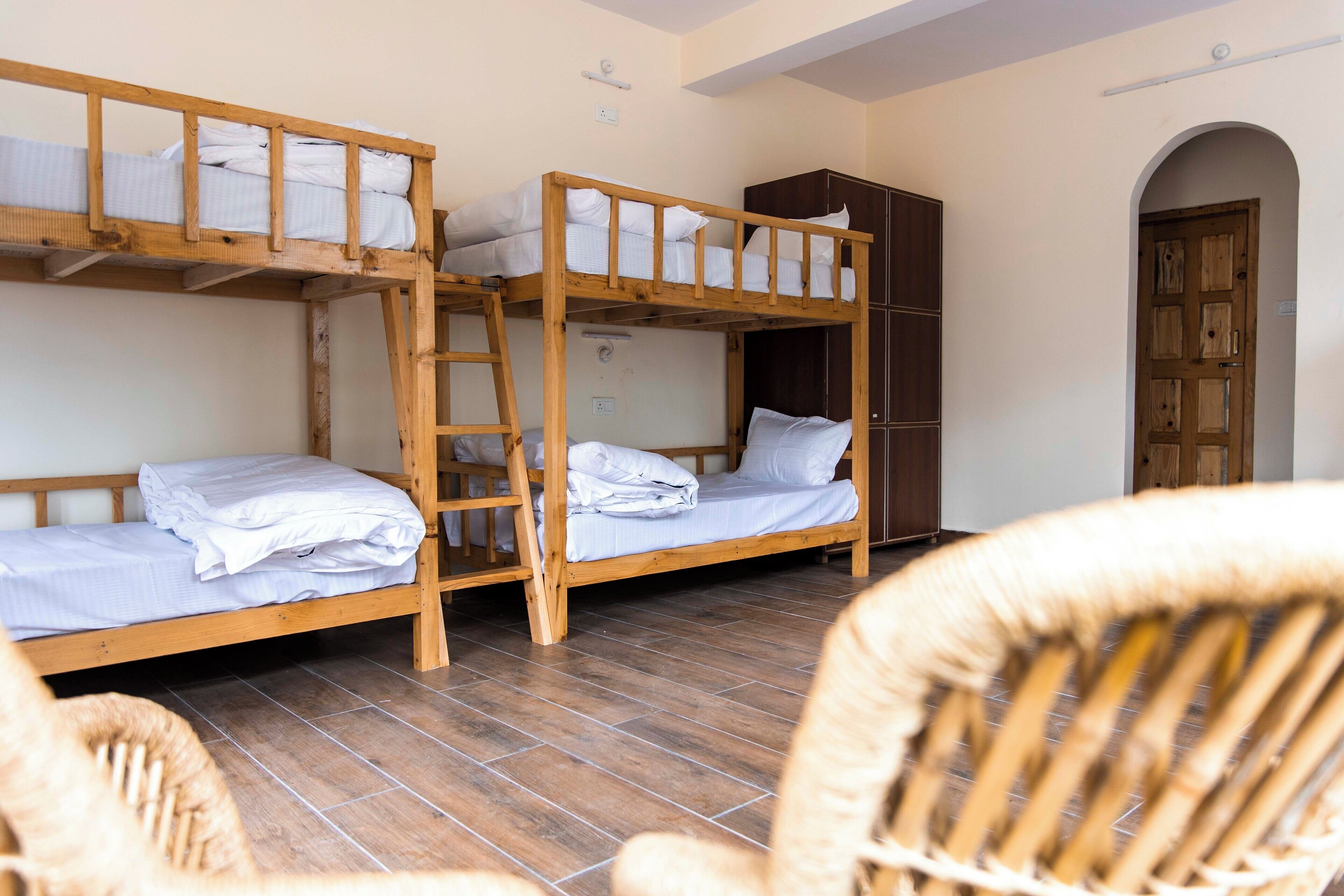 A dormitory room with bunk beds, a wooden wardrobe, and wicker chairs.