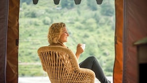 Eine Person sitzt in einem Korbstuhl vor einem Fenster mit Blick auf eine grüne Landschaft.