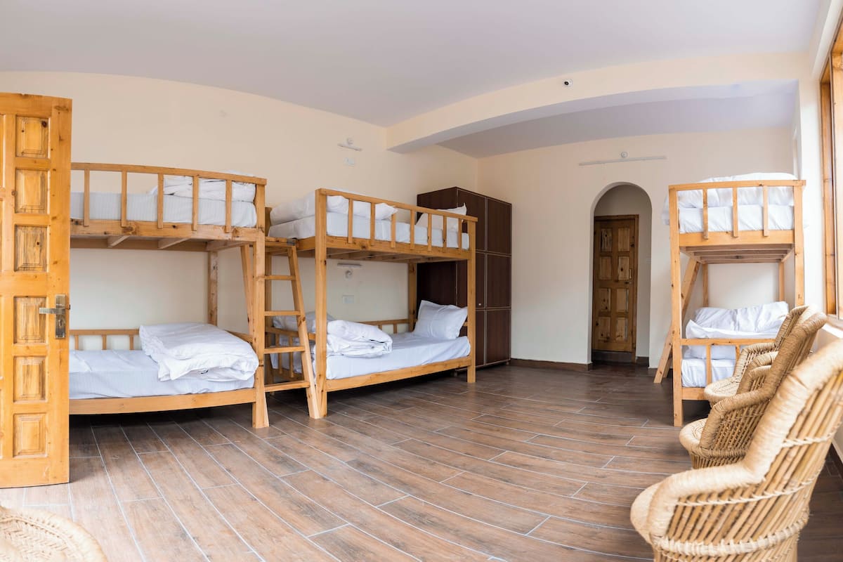A dormitory room with bunk beds, a wardrobe, and a wicker chair.
