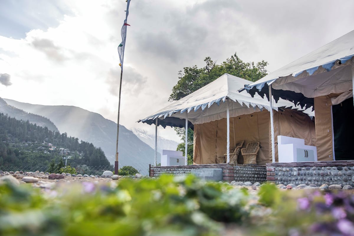 A tented accommodation with a stone wall foundation, a flagpole, and a mountainous backdrop.
