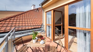 A balcony with a table set for breakfast, a potted plant, and a view of the roof and neighboring buildings. - Modern apartment on Graficka (Prague)