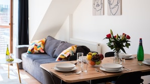 A modern living room with a dining area, grey sofa, colorful pillows, and a vase with flowers. - Modern apartment on Graficka (Prague)