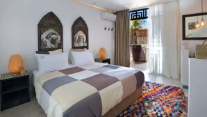 Ein Hotelzimmer mit einem großen Bett, zwei Nachttischen, einem farbenfrohen Teppich und Blick ins Freie.