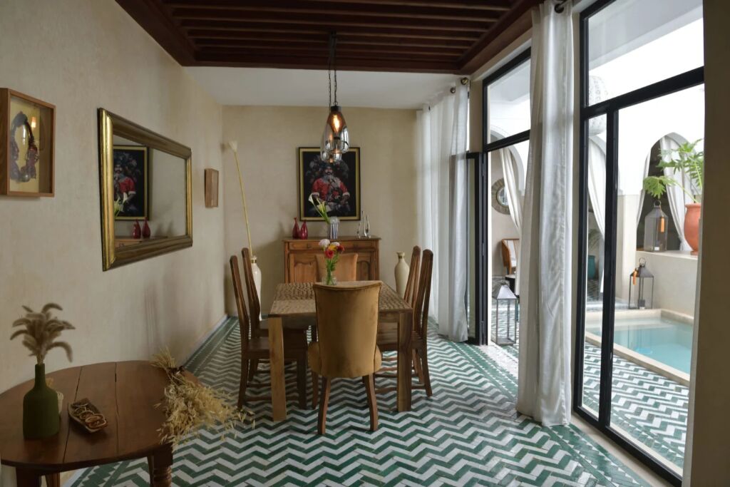 Un espace repas comprenant une table et des chaises, un lustre et une vue sur une piscine, visible à travers de grandes fenêtres.