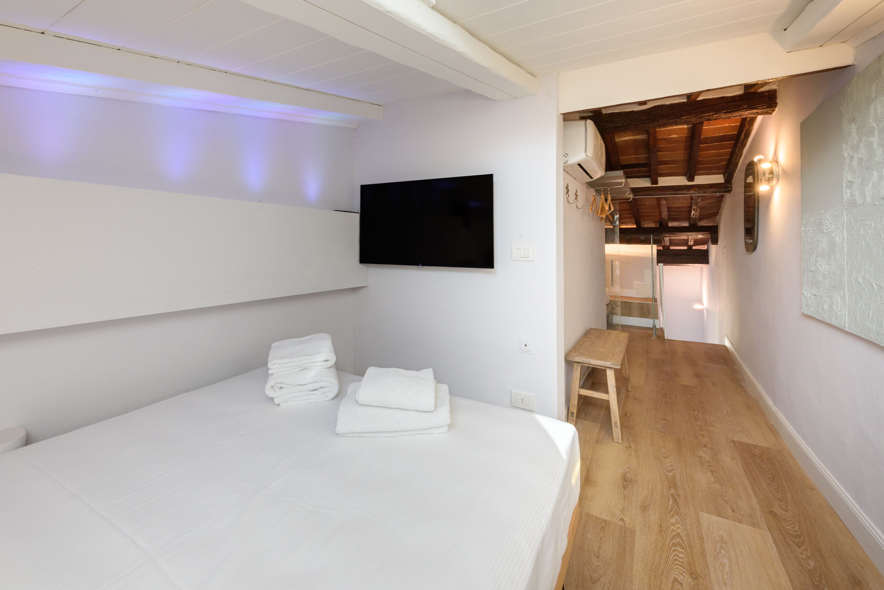 Ein Schlafzimmer mit einem Bett, einem Flachbildfernseher, einer hölzernen Bank und einem Flur, der zu einem Badezimmer führt.