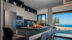 A modern kitchen with a central island, bar stools, and a view of the sea. - Nikolakos Villa - pirvate pool (Zakinthos)