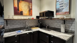 Una cucina moderna con mobili in legno scuro, un piano di lavoro in granito, un forno a microonde e un grande quadro astratto appeso alla parete.