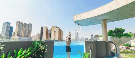A rooftop pool with a cityscape view, surrounded by potted plants.