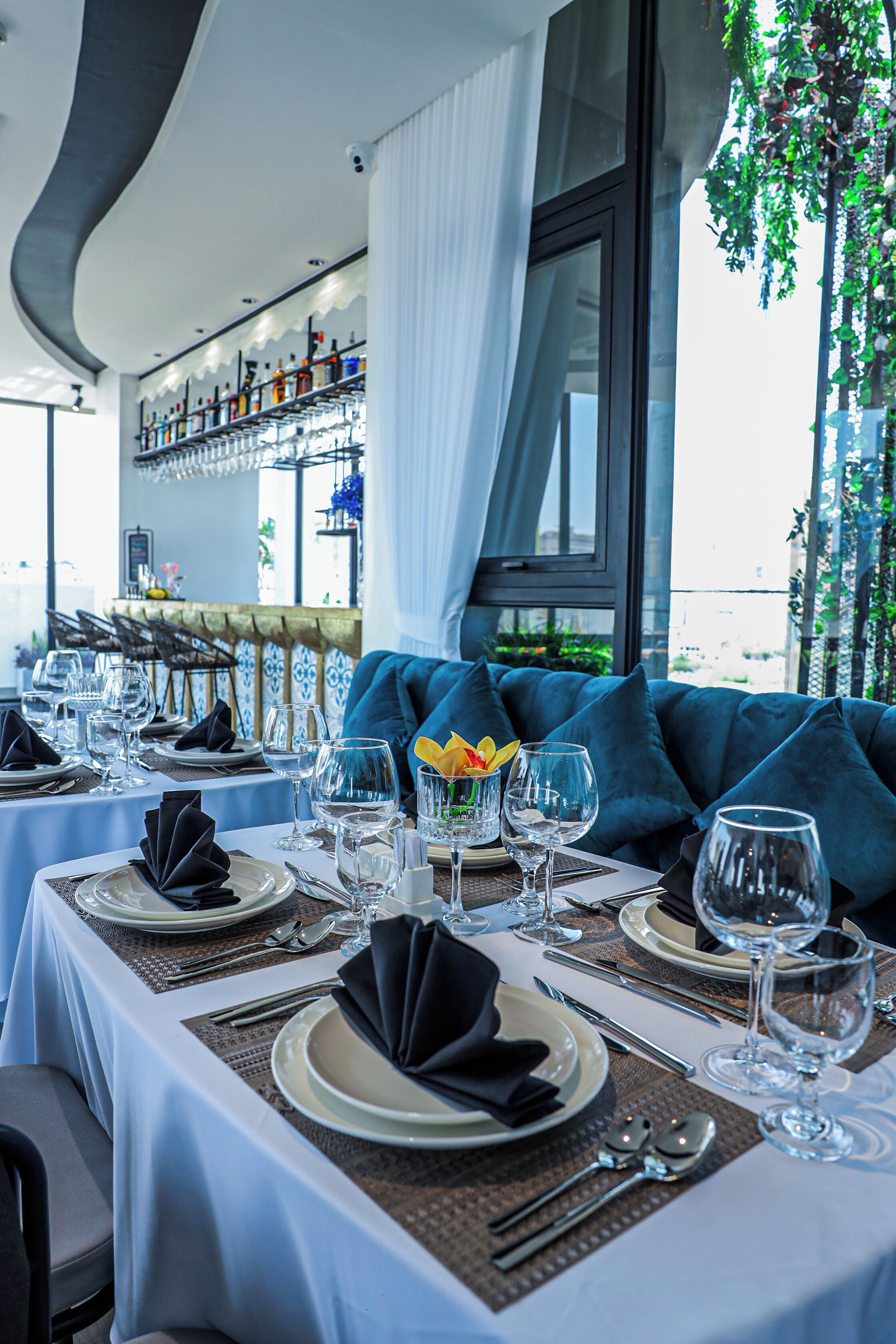 A dining area with tables set for a meal, featuring white tablecloths, neatly arranged plates, glasses, and cutlery.