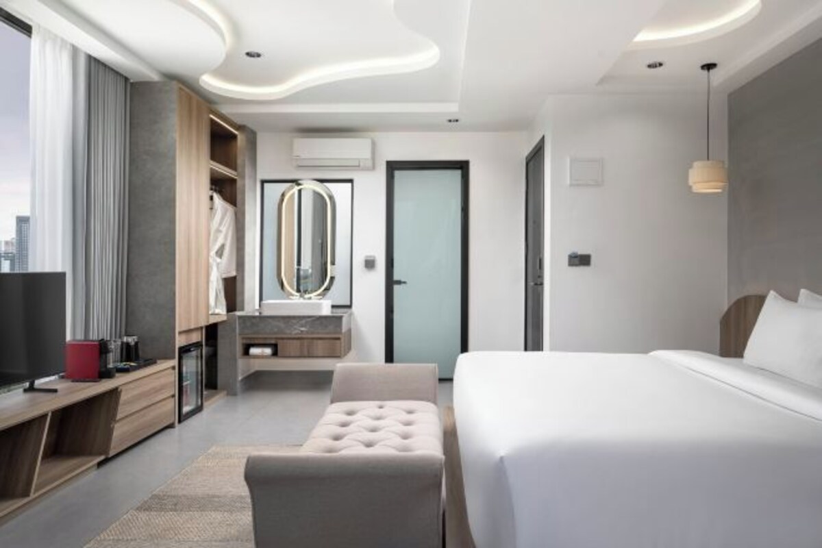 Una habitación de hotel moderna con una cama grande, un área de descanso, una tocador con espejo y un televisor.