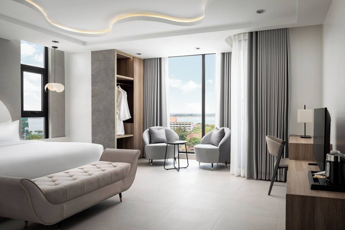 Moderni hotellihuone, jossa on suuri sänky, kaksi nojatuolia, pieni pöytä, televisio ja vaatekaappi.