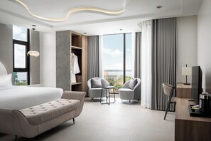 Habitación de hotel moderna con una cama grande, dos sillones, una mesita, un televisor y un armario.