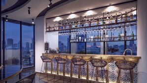 Zona de bar con vista a la ciudad, taburetes y una variedad de botellas y vasos.