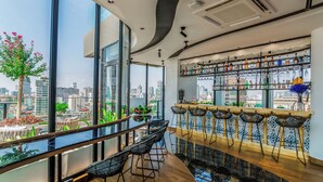 Zona de bar moderna con vistas a la ciudad, amplias ventanas y diversas opciones de asientos.