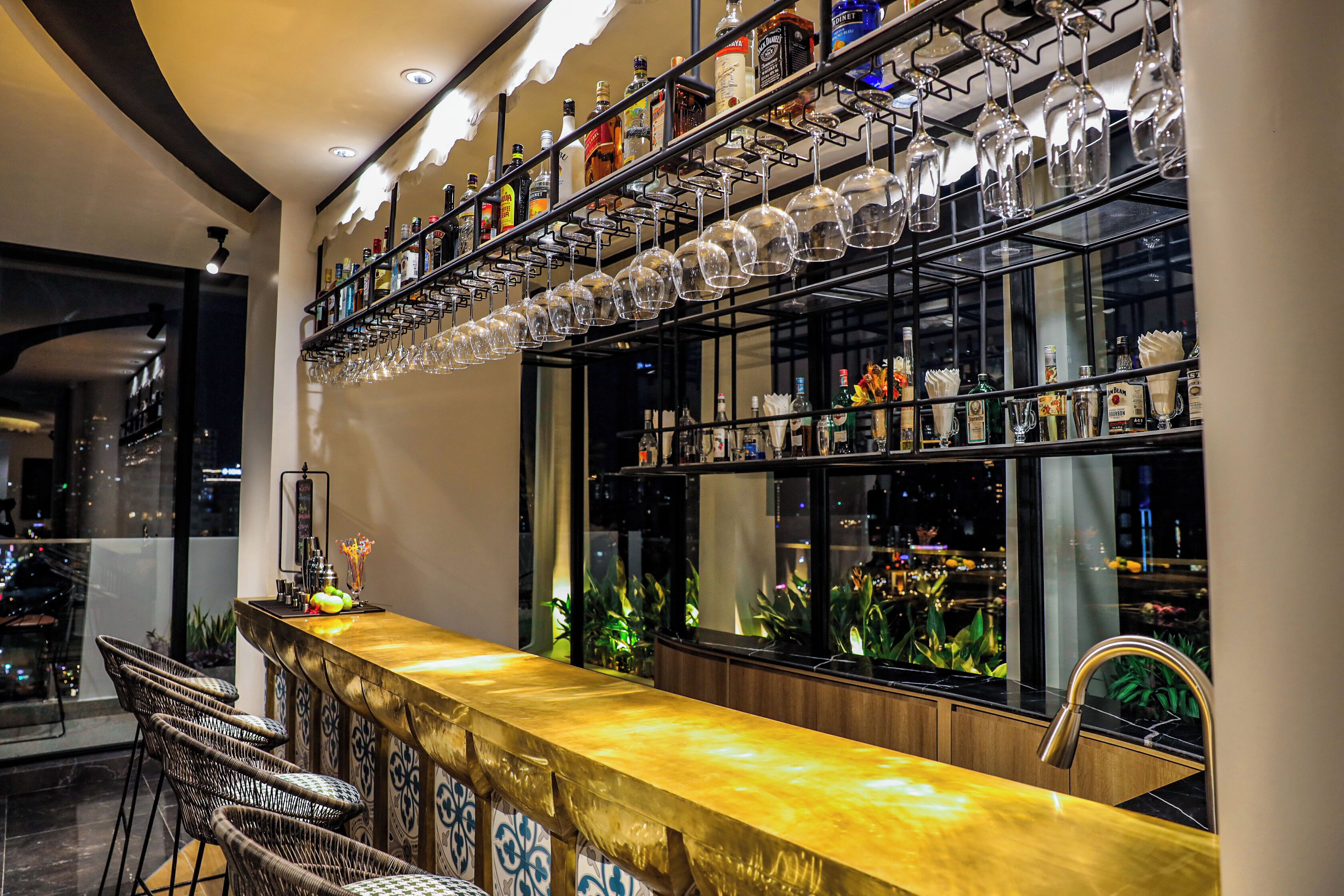 A bar area with a long counter, multiple shelves of bottles, and hanging wine glasses.
