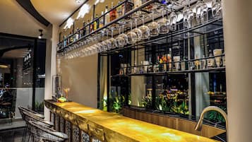 A bar area with a long counter, multiple shelves of bottles, and hanging wine glasses.